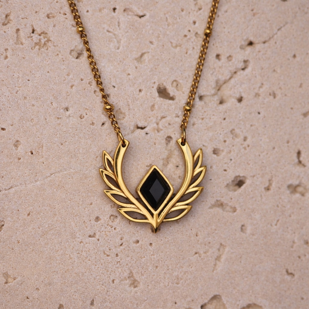 Gold necklace with a black pendant on a beige stone surface