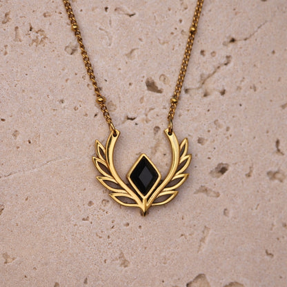 Gold necklace with a black pendant on a beige stone surface