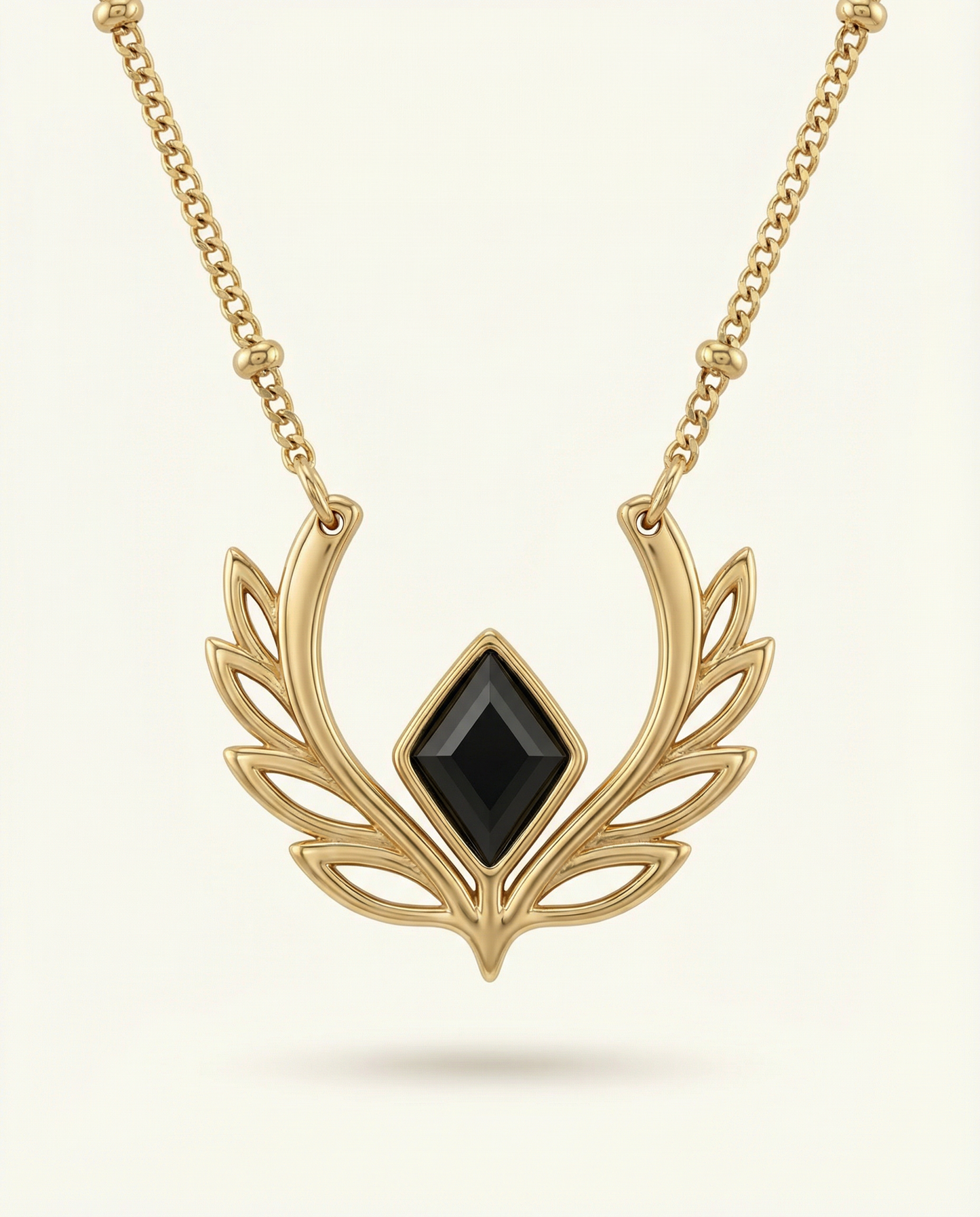 Gold necklace with a black gemstone on a light beige background