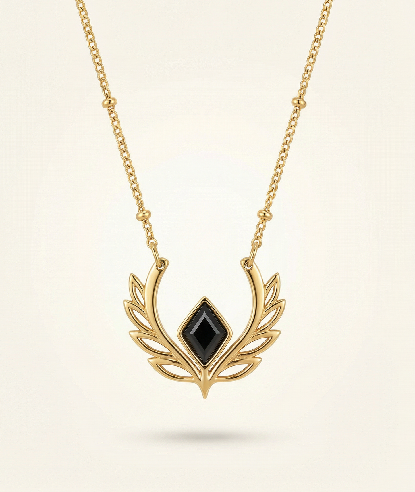 Gold necklace with a black gemstone pendant on a beige background