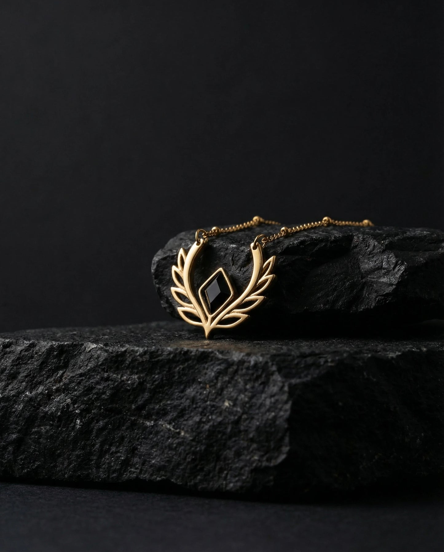 Gold necklace with a black pendant on a dark stone surface